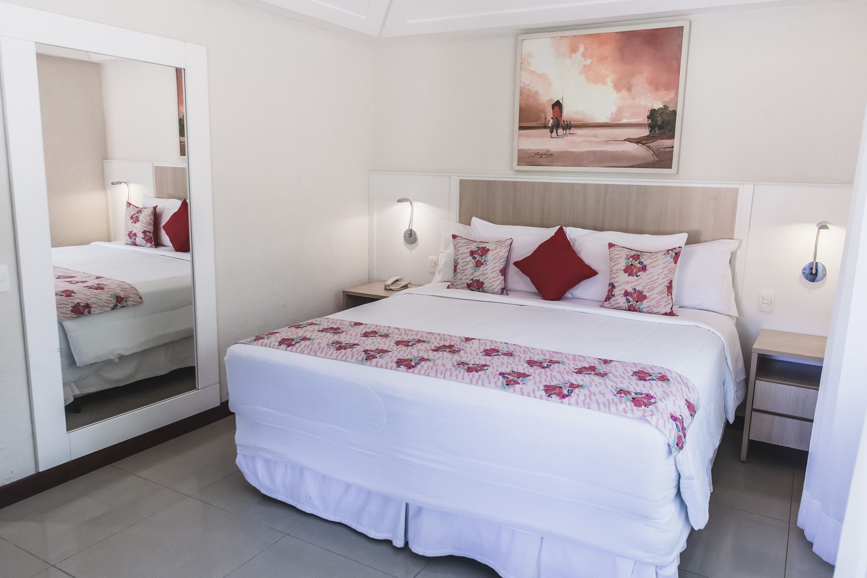 Un dormitorio con una cama grande, un espejo, lámparas de noche y un cuadro en la pared.