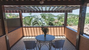 Un balcón cubierto con una mesa y sillas, una planta en maceta y vistas de un paisaje costero.
