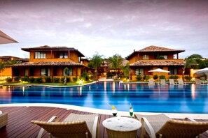 Piscina com espreguiçadeiras e uma mesa, cercada por edifícios com telhados em azulejo.