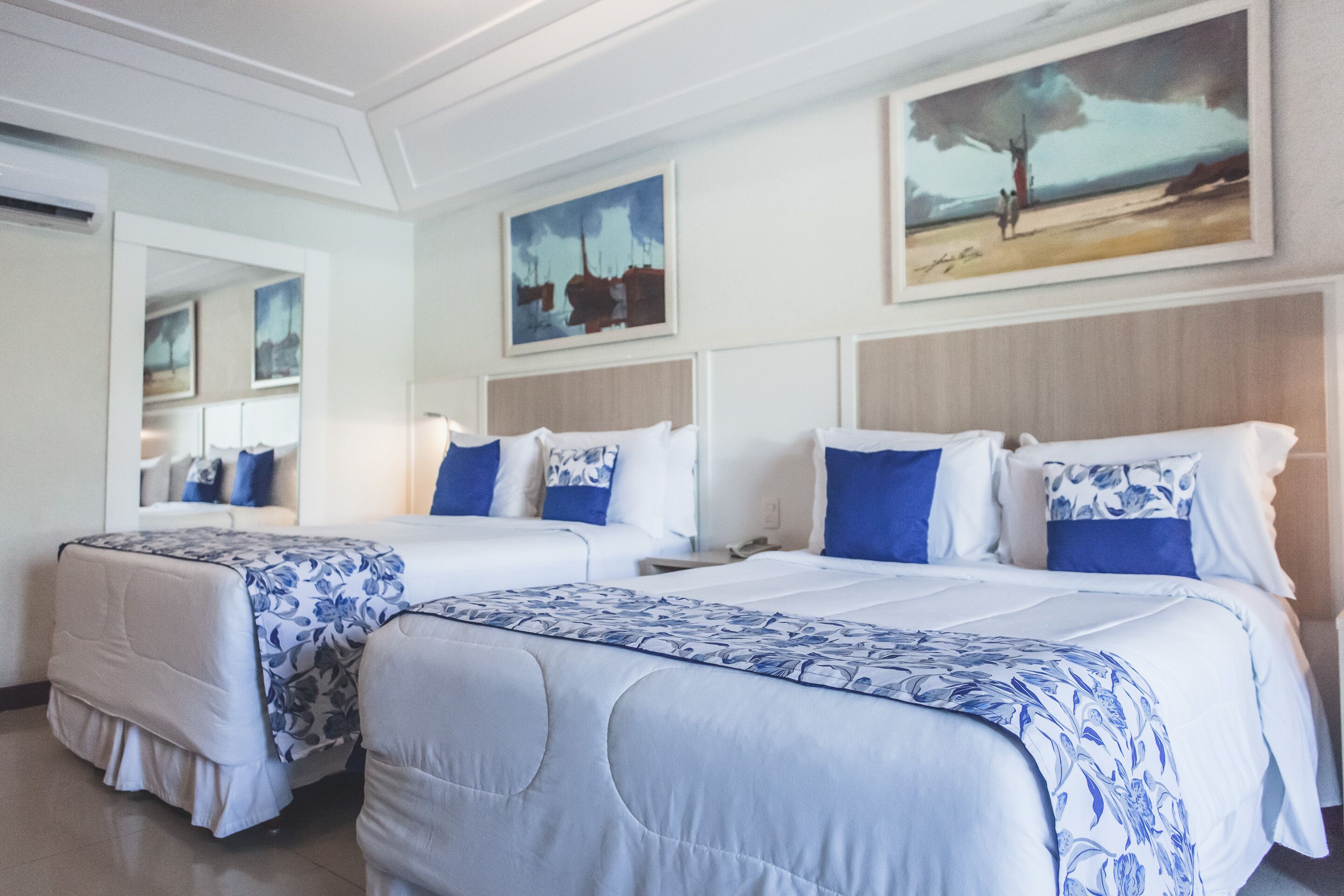 A hotel room with two beds, a large mirror, and artwork on the walls.