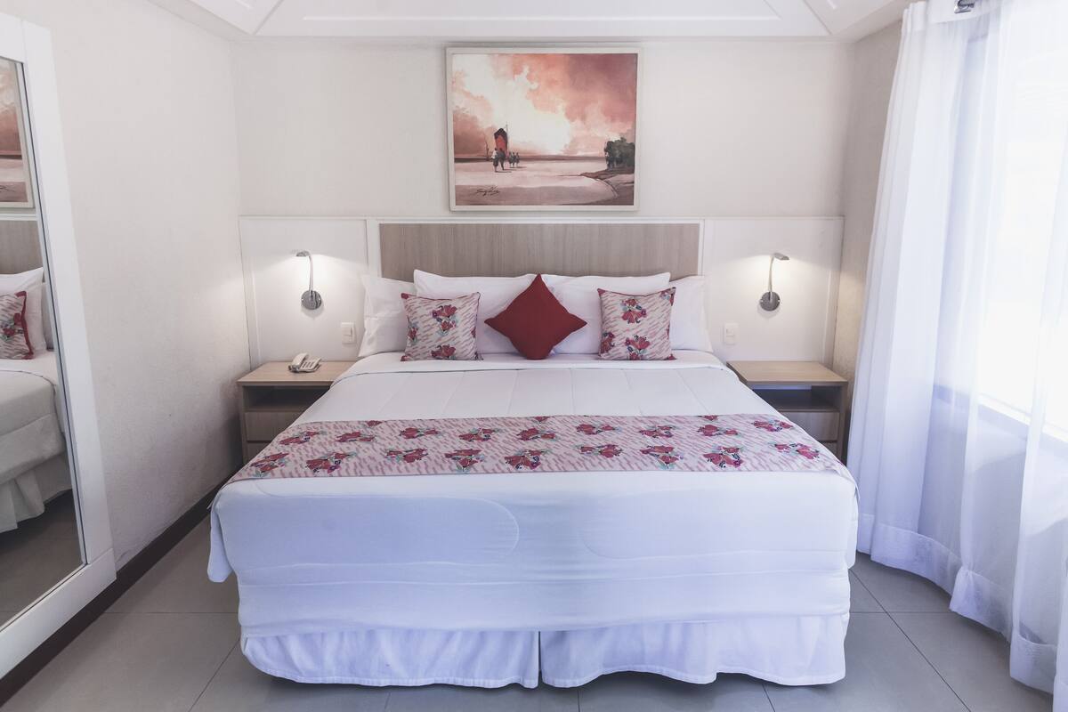 Une chambre d’hôtel avec un grand lit, deux tables de chevet, une commode, un miroir et un tableau au mur.