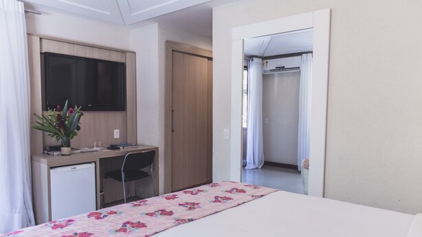 Habitación de hotel con cama, escritorio, computadora, televisión y zona de ducha.