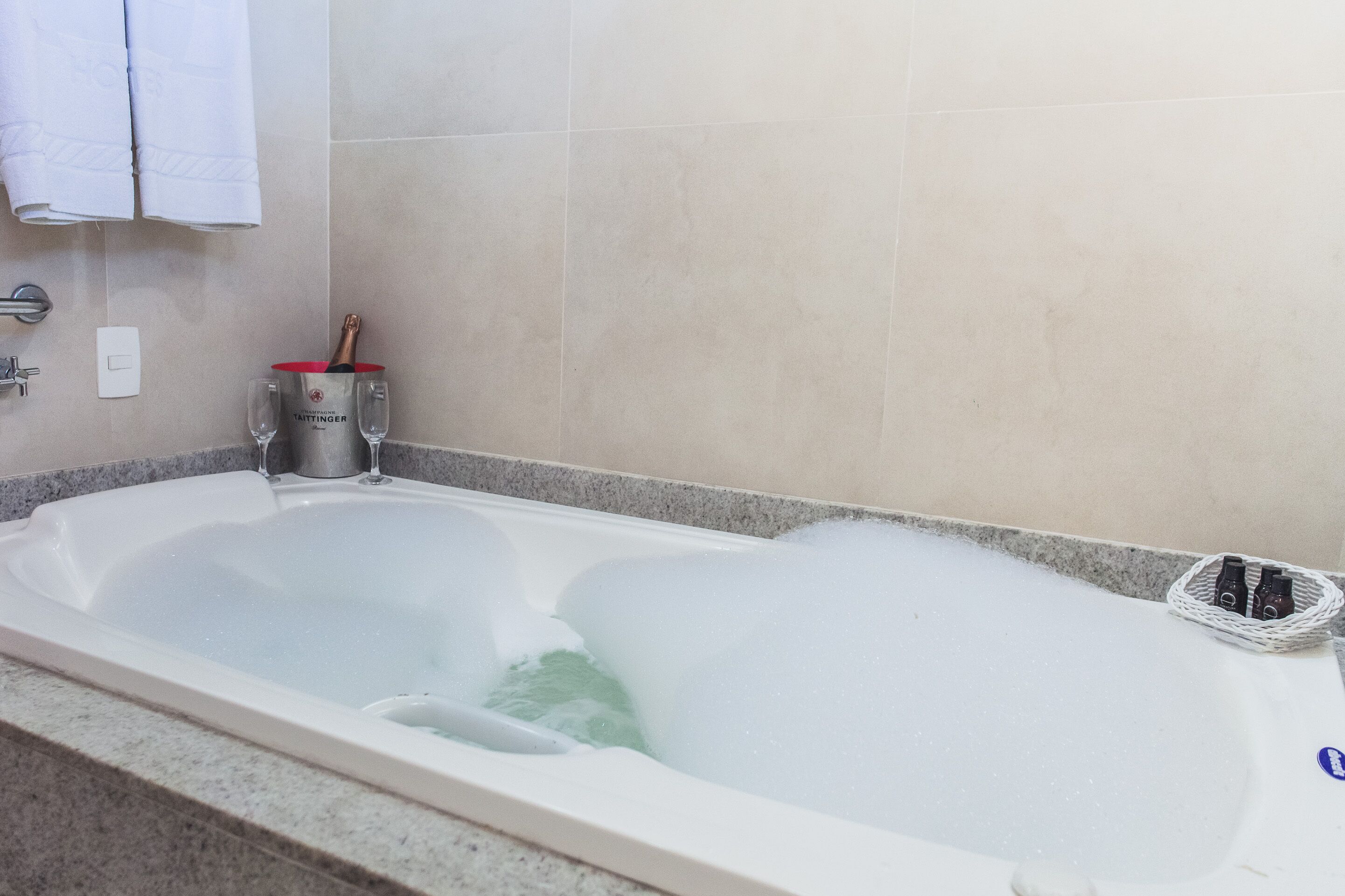 A bathtub filled with bubbles, a bottle of champagne, and two glasses on the side.