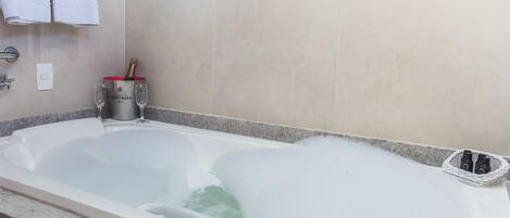 A bathtub filled with bubbles, a bottle of champagne, and two glasses on the side.