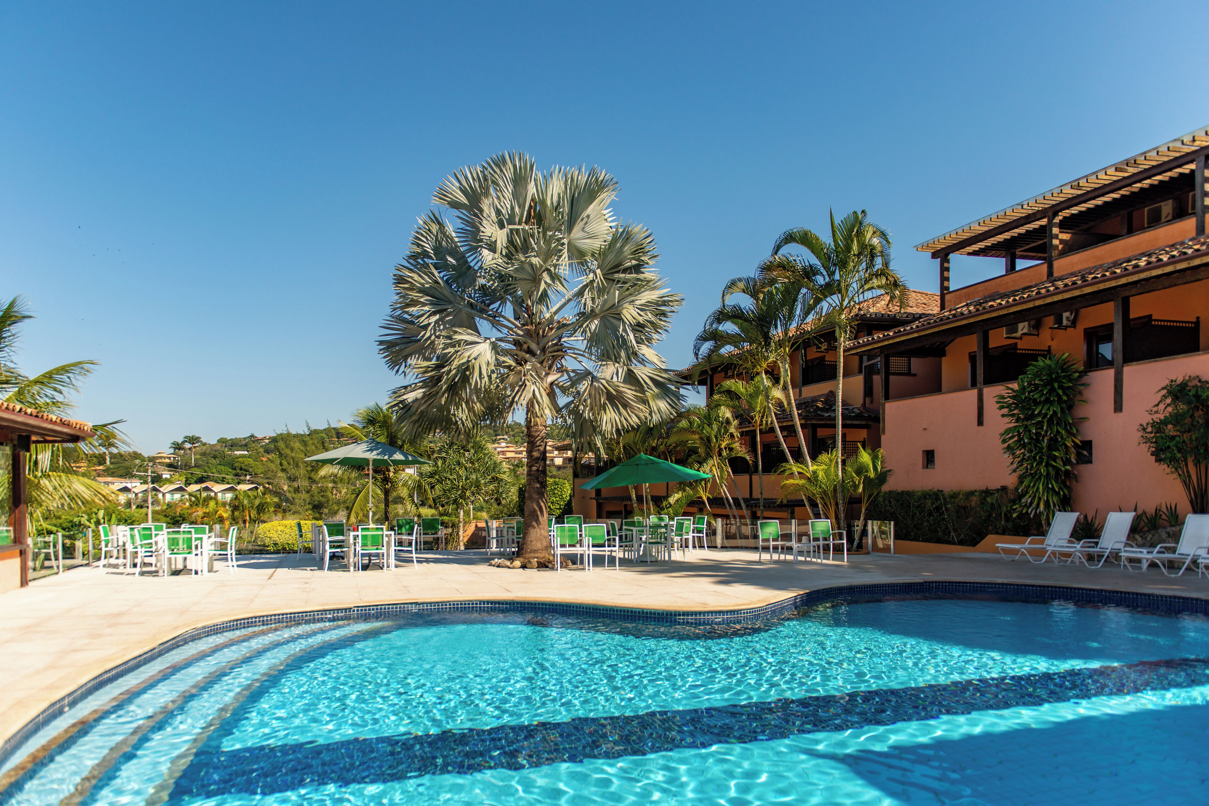 A swimming pool with clear blue water, surrounded by lounge chairs and palm trees.
