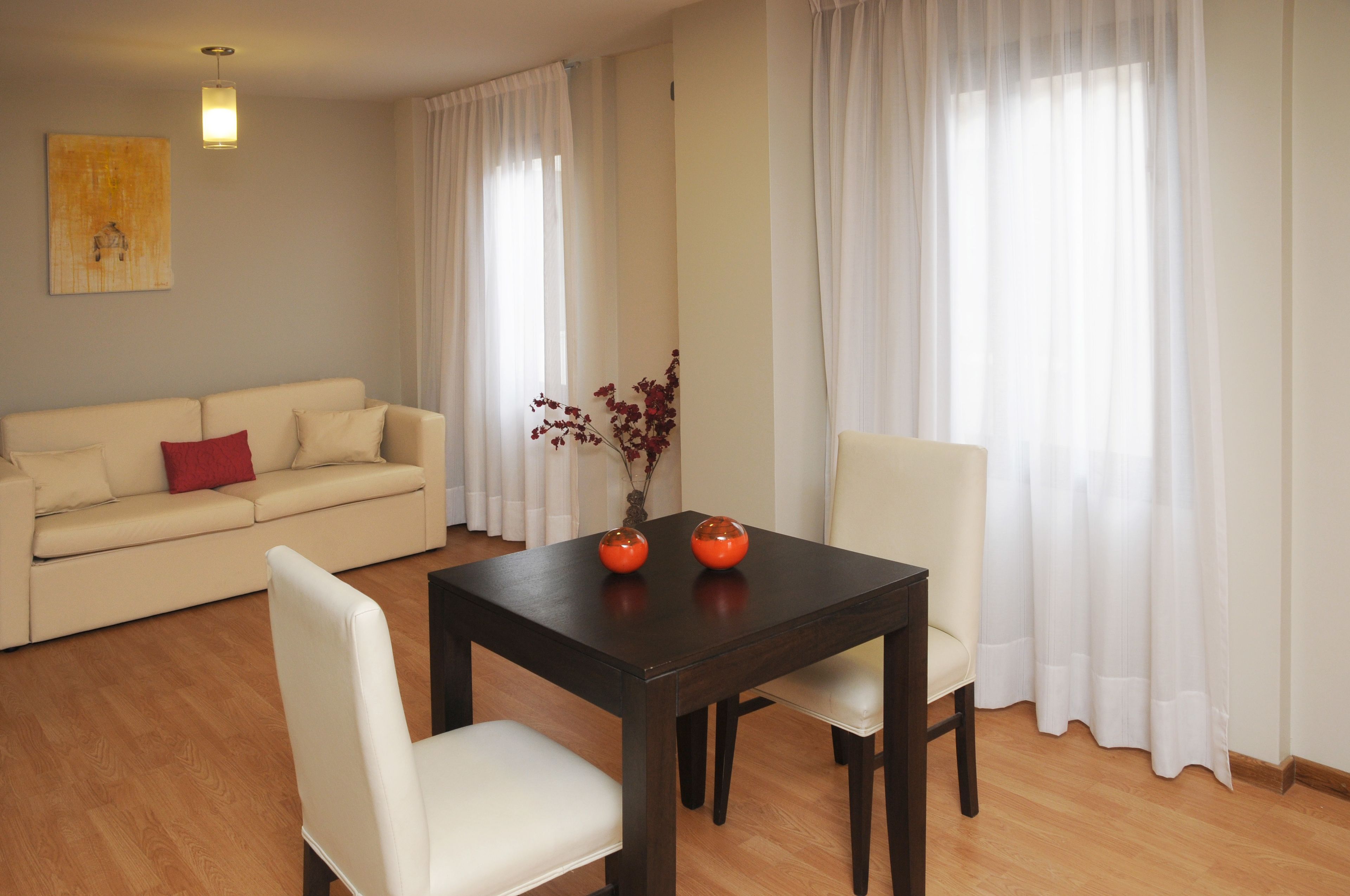A living room with a sofa, a dining table with two chairs, and a vase with flowers.