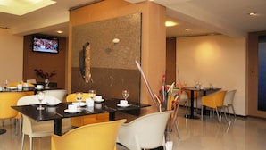 A modern dining area with tables and chairs, a television mounted on the wall, and a decorative wall piece. - Del Bono Suites Art Hotel (San Juan)