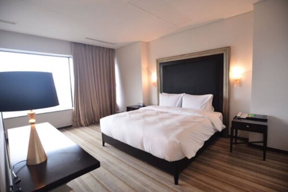 A hotel room with a large bed, a bedside table, a lamp, and a window with curtains.
