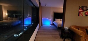 A hotel room with a large window, a bed, a sofa, and a painting on the wall. - Hotel Philos (Pohang)
