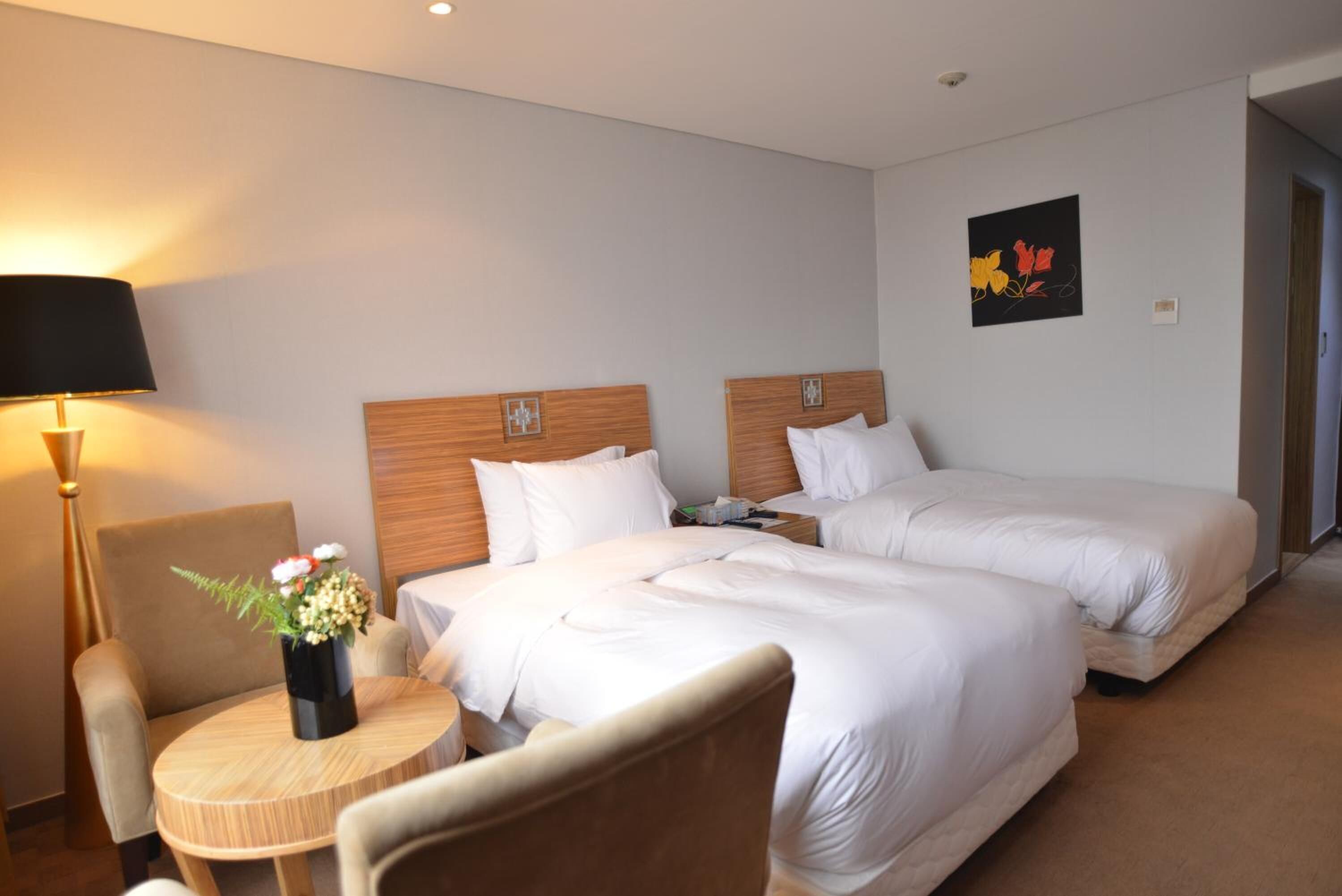 A hotel room with two beds, a round wooden table, a chair, and a lamp.
