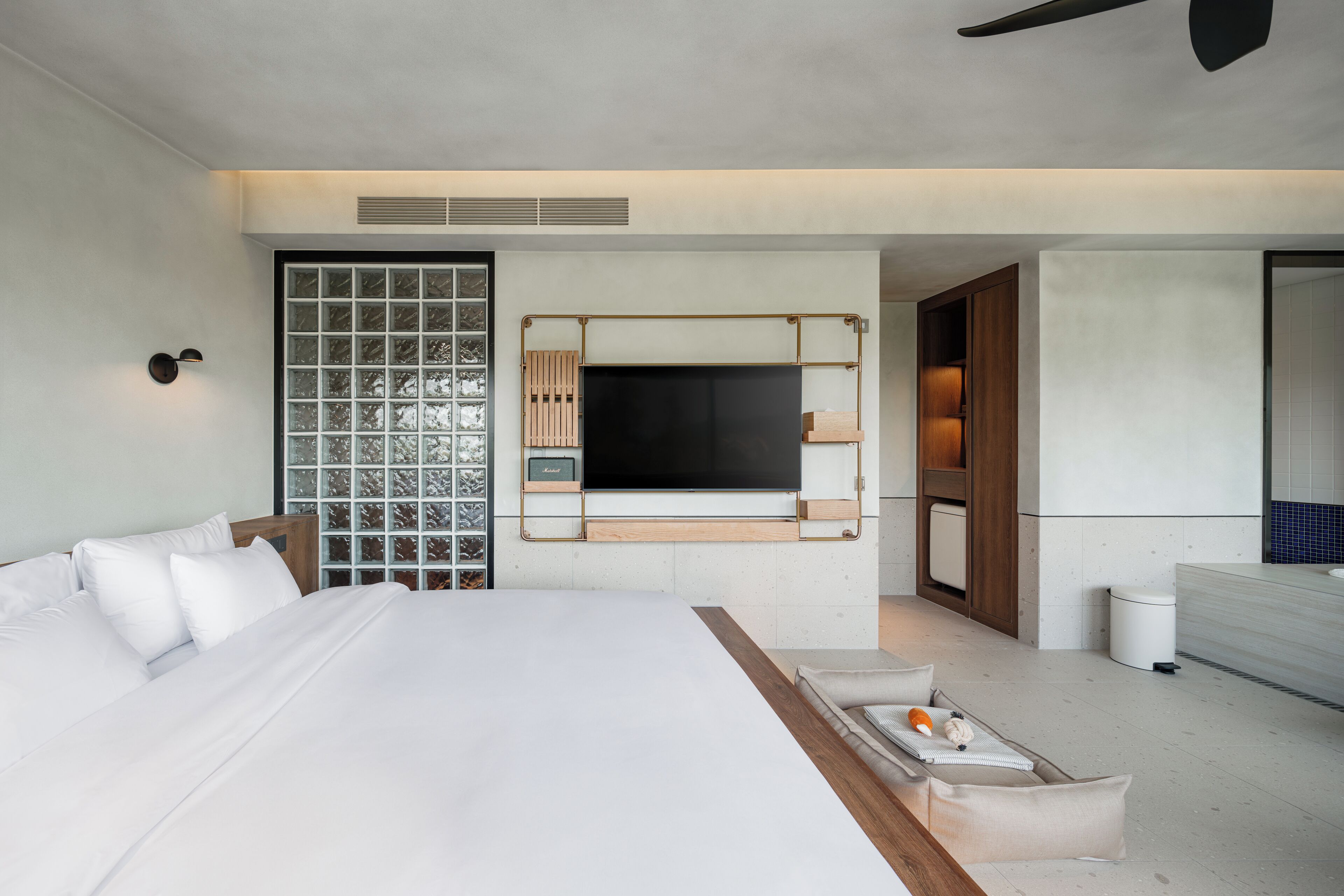 A modern hotel room with a large bed, a TV mounted on the wall, a small seating area, and a bathroom visible through an open door.