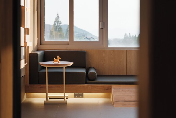A modern room with a wooden floor, a black sofa with a wooden side table, and a view of a mountain through a large window. - KINOCK Pet Hotel (Gyeongju)