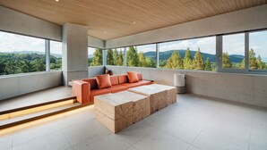 Ein modernes Wohnzimmer mit großem Fenster, Holzbalkendecke und einer Couch mit orangefarbenen Kissen.
