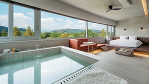 Ein modernes Schlafzimmer mit großem Fenster, einer Badewanne, einem Bett und einer Sitzecke.