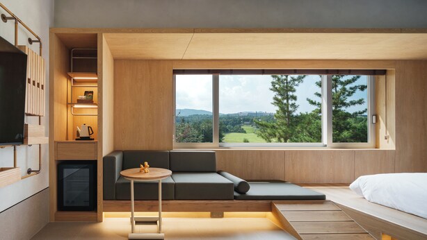 Ein modernes Zimmer mit einer eingebauten Couch, einem kleinen Tisch und einem Bett. Ein großes Fenster bietet Blick auf Grünflächen und Hügel.