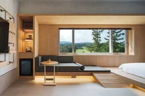 A modern room with a built-in sofa, a small table, and a bed. There is a large window offering a view of greenery and hills. - KINOCK Pet Hotel (Gyeongju)
