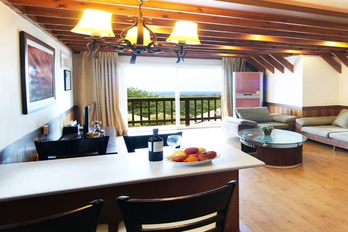 Una sala moderna con un sofá, una mesa de comedor con sillas, una mesa de centro de vidrio y una zona de cocina con un refrigerador.