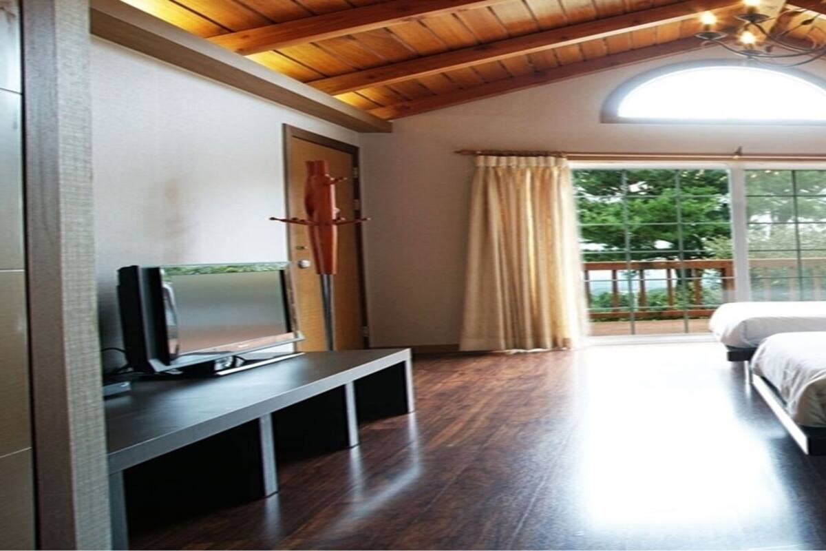 Habitación de hotel con techo de madera, un ventanal con cortinas, cama, escritorio con frutero y televisor.