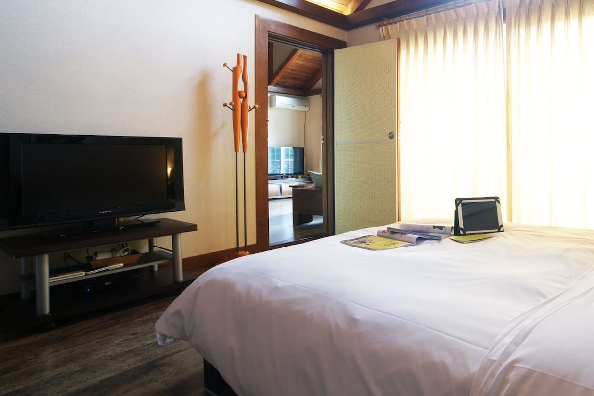 Habitación de hotel con cama, televisión, mesita de noche con lámpara y ventana con cortinas.