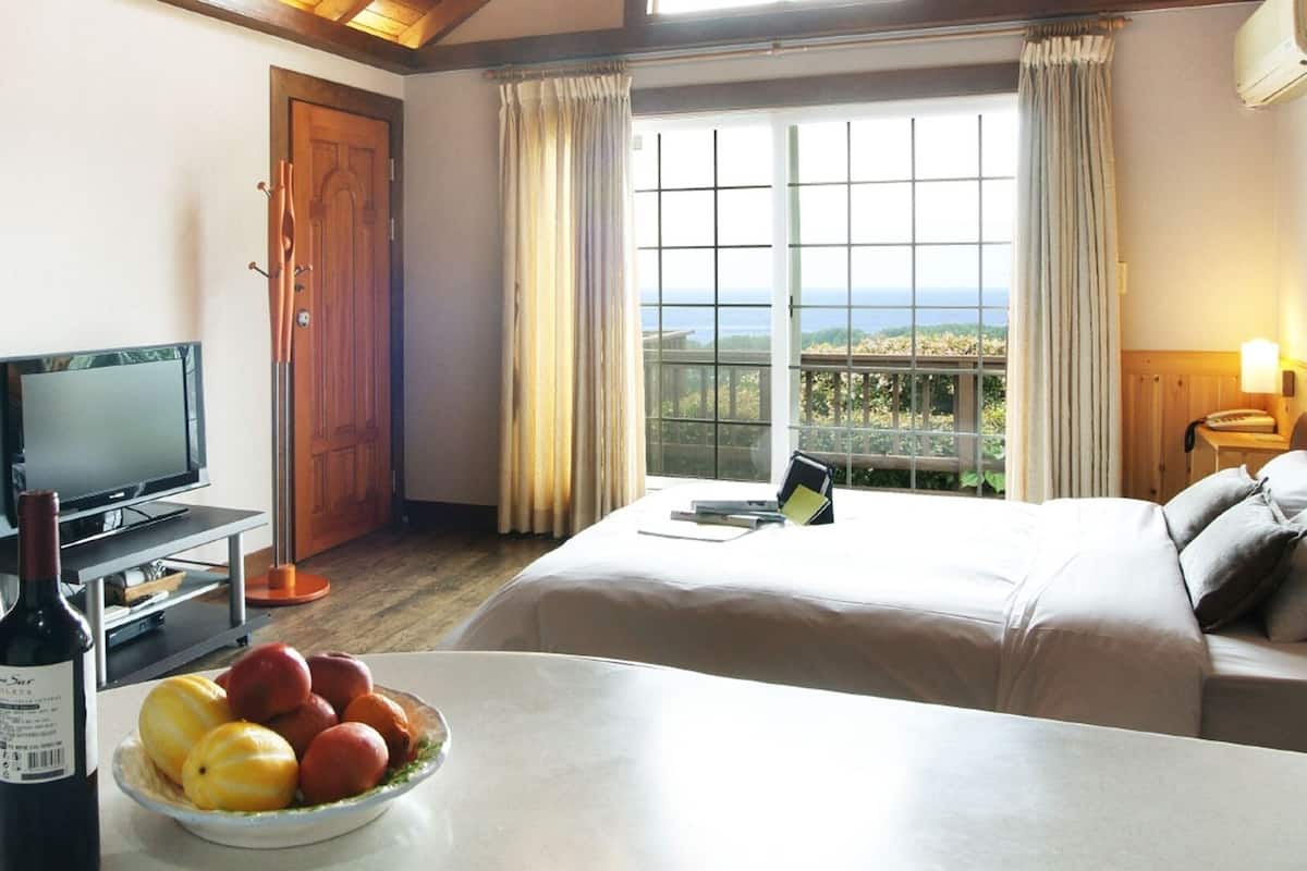 Habitación de hotel con cama, televisión, mesa de comedor con fruta y vista al mar.