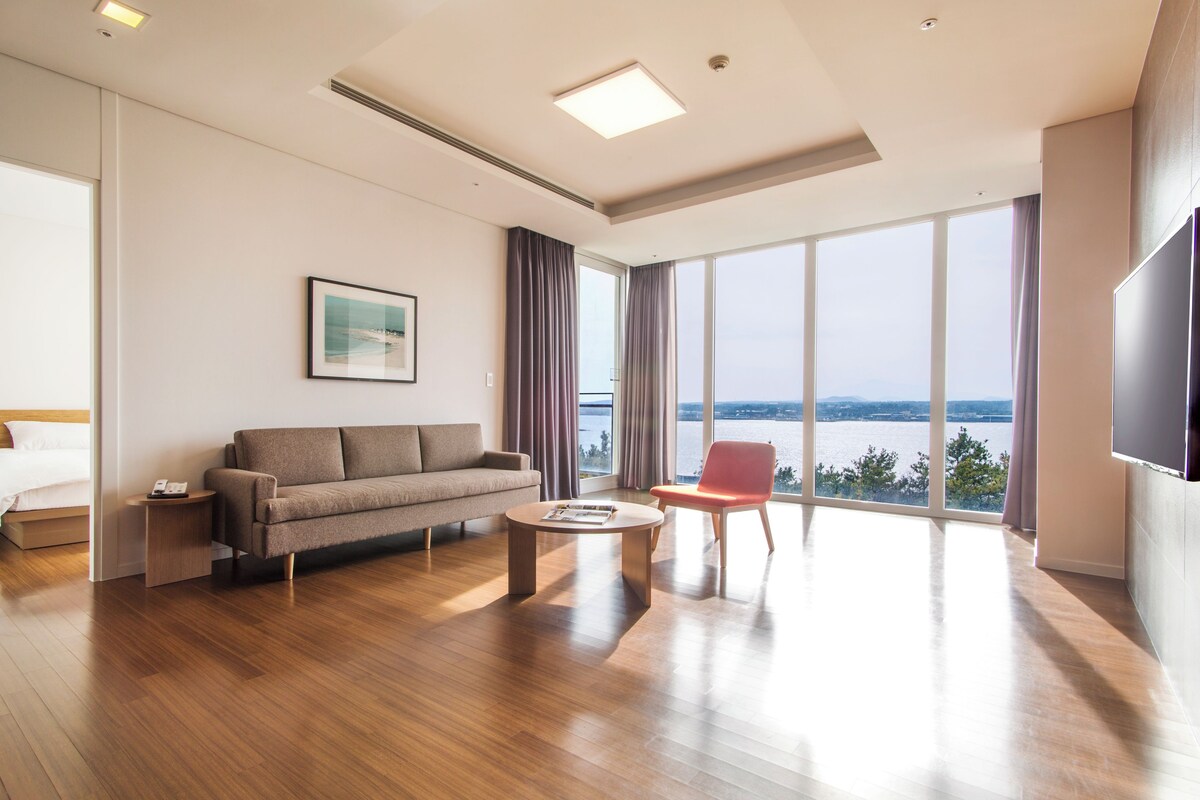 Una habitación de hotel moderna con un ventanal grande, un sofá, una mesita de centro y un televisor.