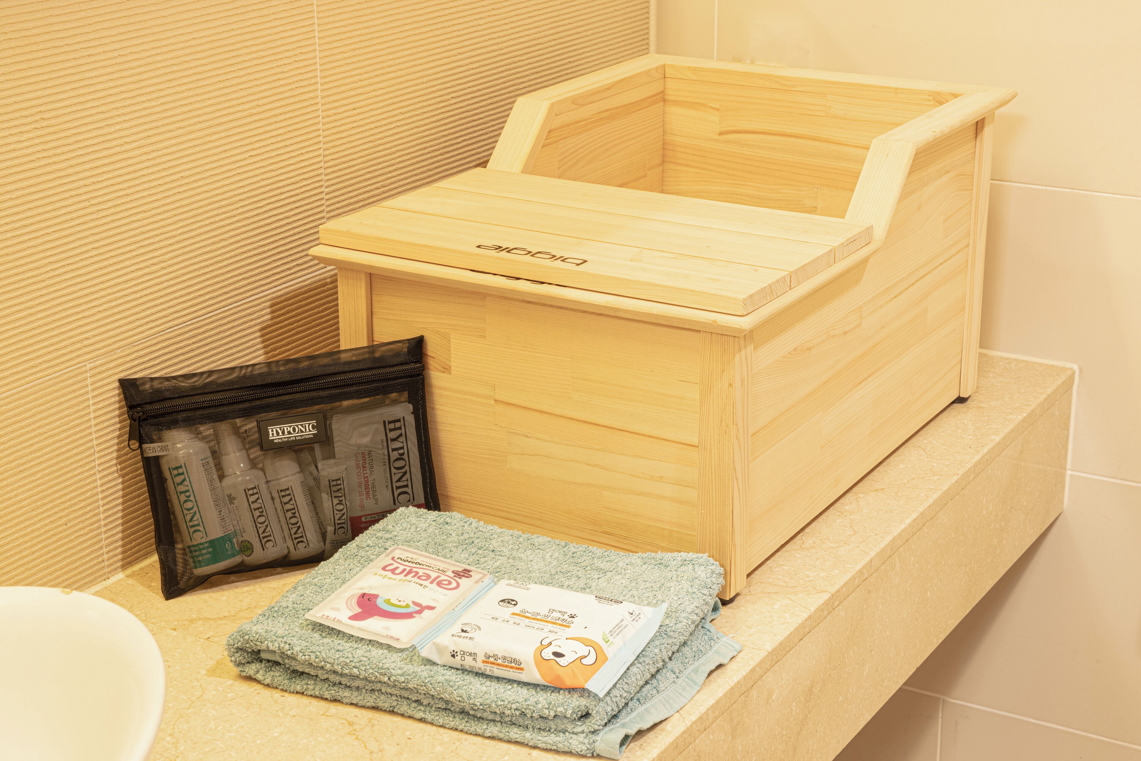 A wooden box with a label, a black bag with items, and a folded towel on a bathroom counter.