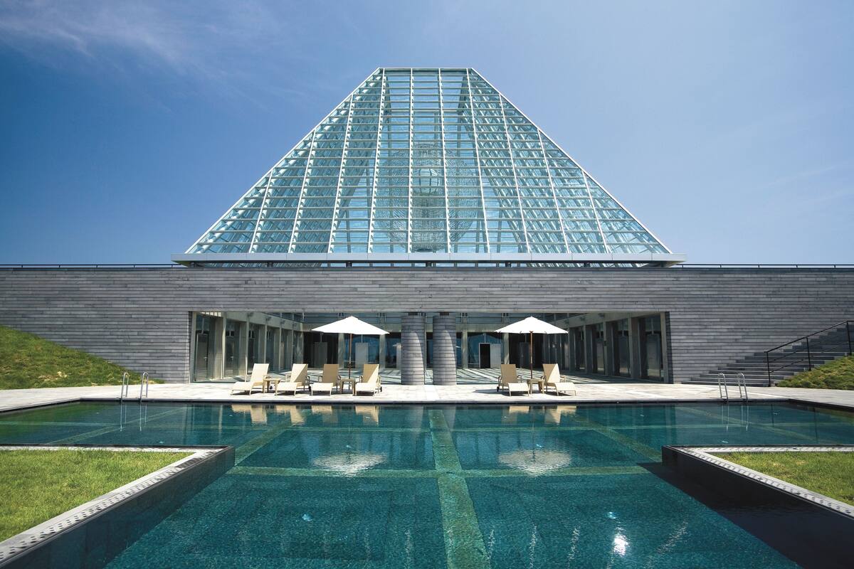 A modern building with a large glass facade, a swimming pool, and lounge chairs.