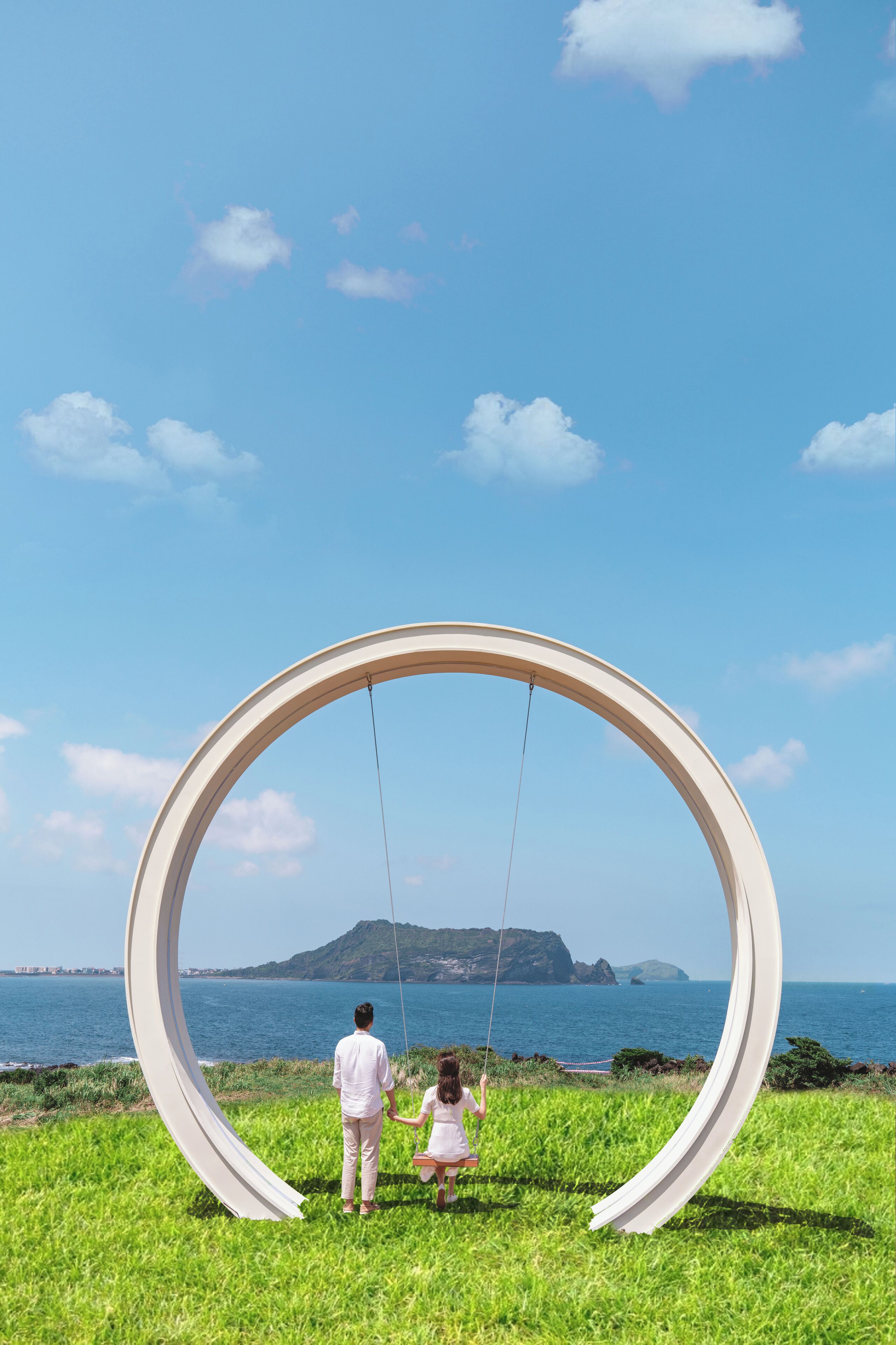A couple on a swing with a circular frame, overlooking a body of water and distant landforms.