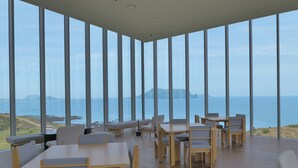 A spacious dining area with high ceilings and large windows offering a view of the sea and distant land. - Phoenix Island (Seogwipo)