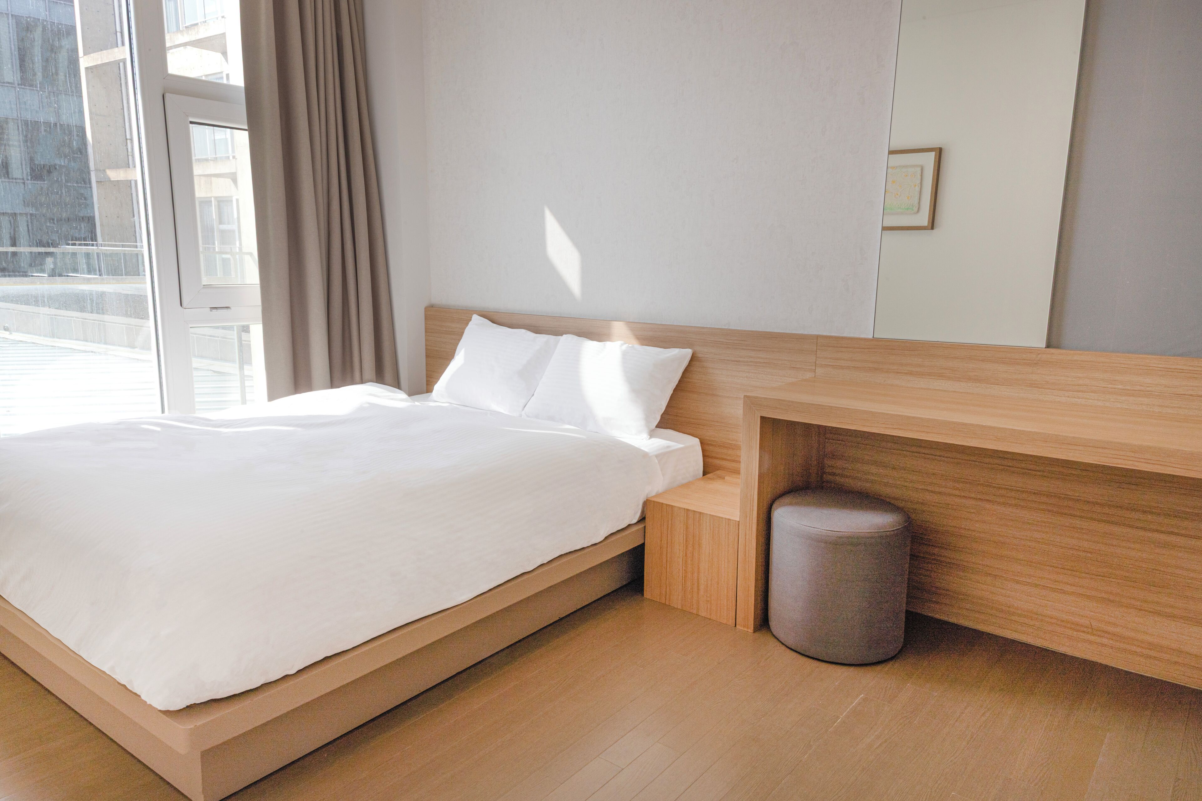 A modern bedroom with a wooden bed frame, a small bedside table, and a grey waste bin.
