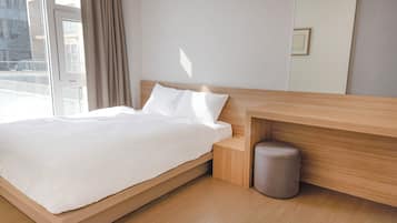 A modern bedroom with a wooden bed frame, a small bedside table, and a grey waste bin.