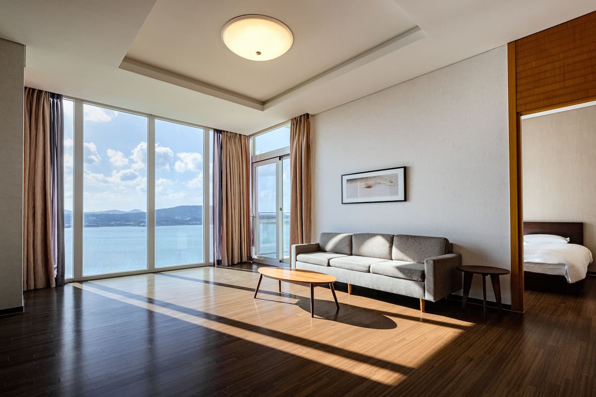 A modern hotel room with a large window, a sofa, a small table, and a bed.