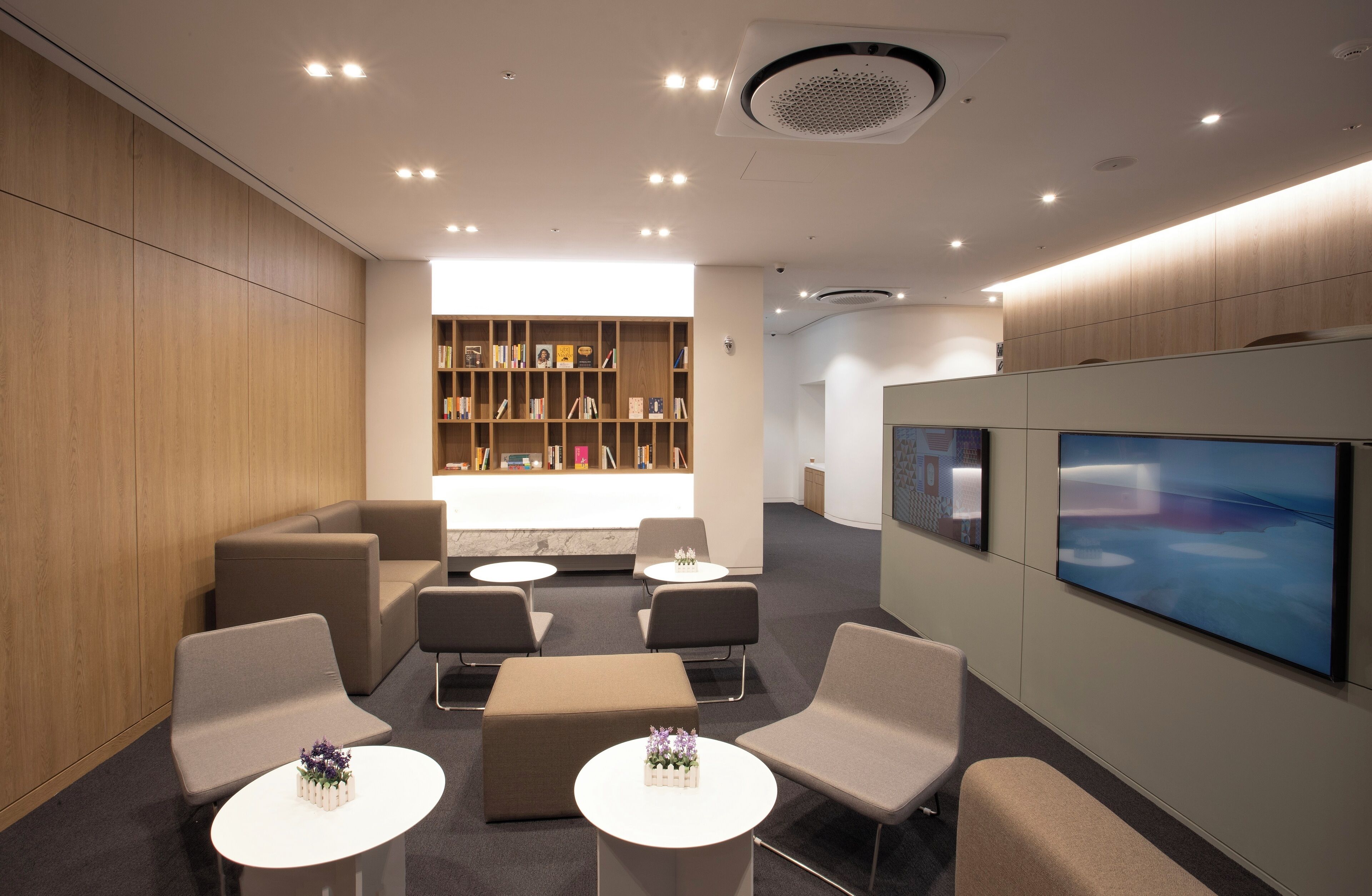 A modern lounge area with seating, a bookshelf, and a large screen.