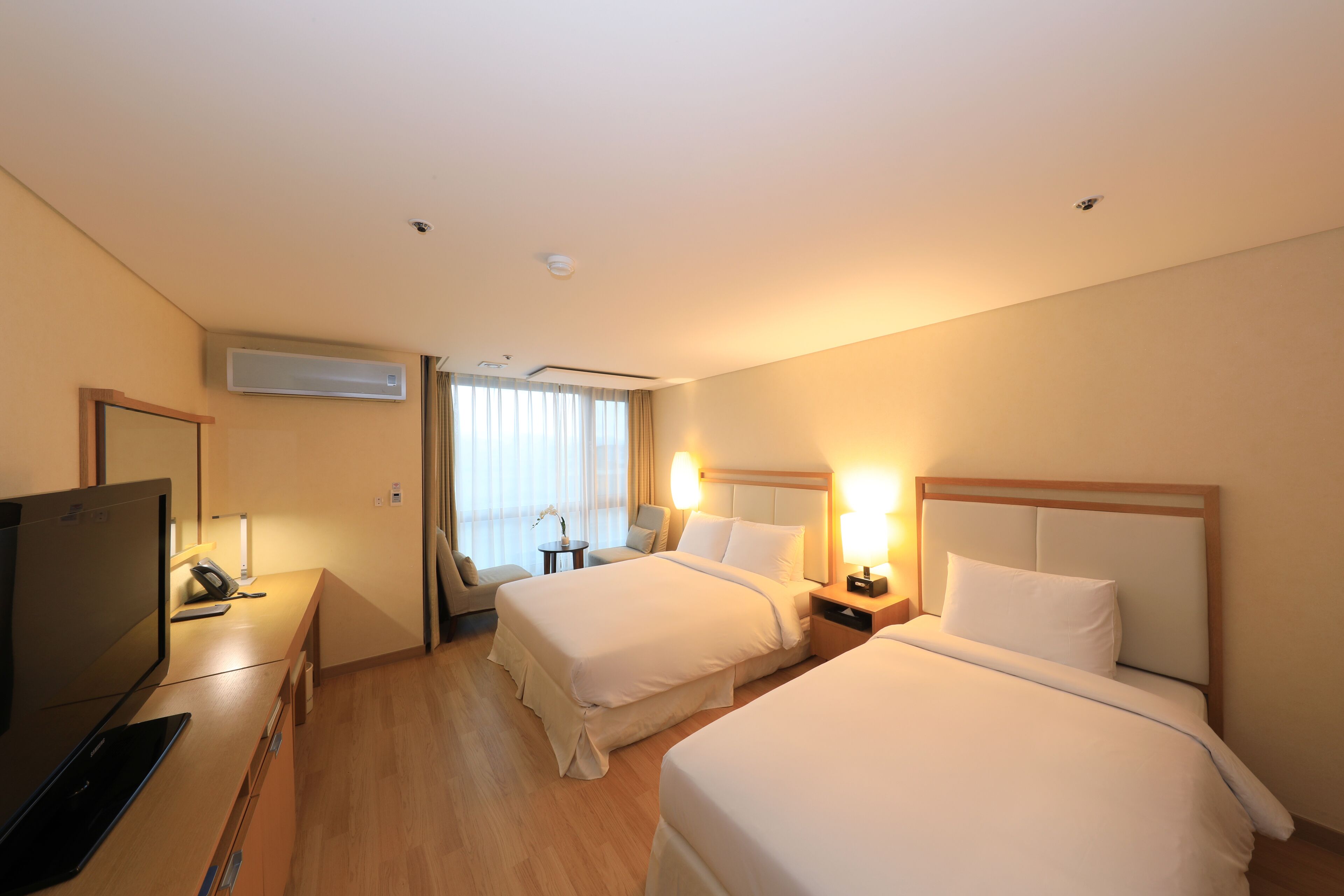 Habitación de hotel con dos camas, un escritorio con ordenador, televisor y ventana con cortinas.