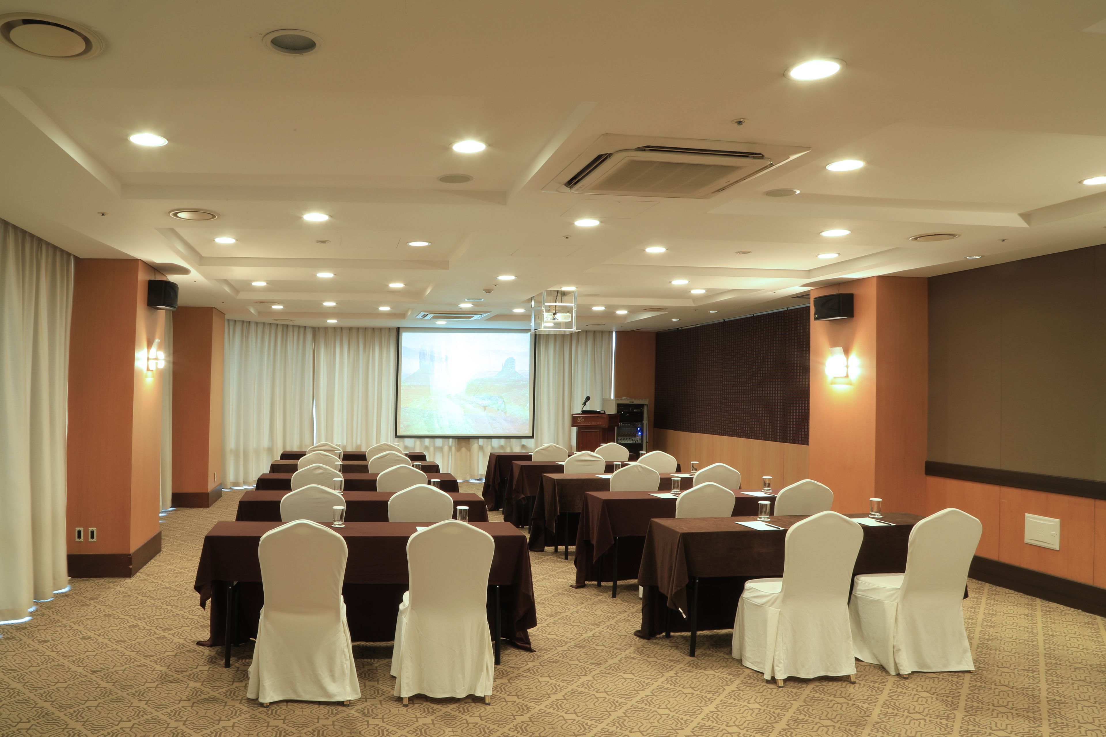 A conference room with rows of tables and chairs, a projector screen, and a podium.
