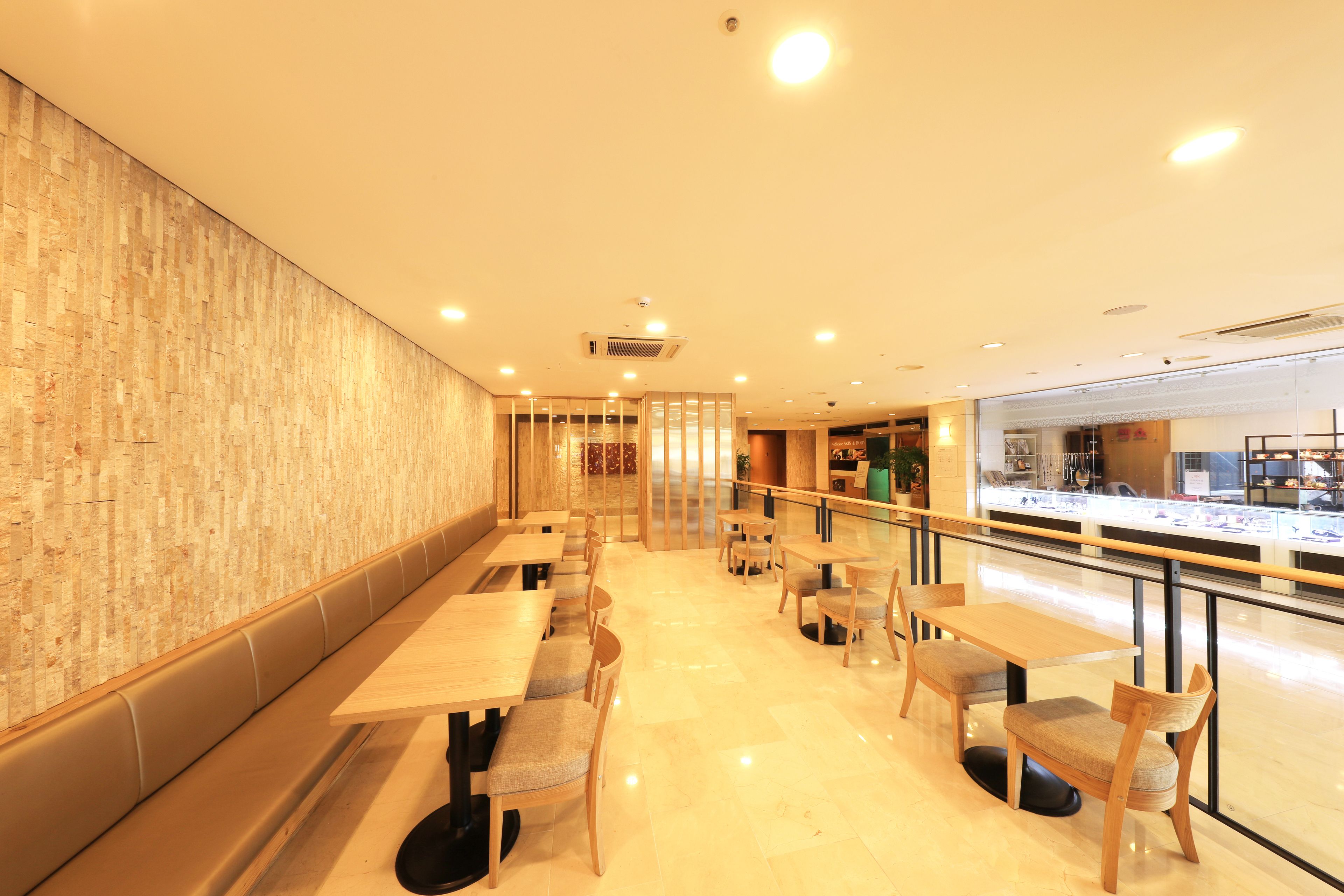 A modern restaurant interior with wooden tables and chairs, a glass partition, and a polished floor.