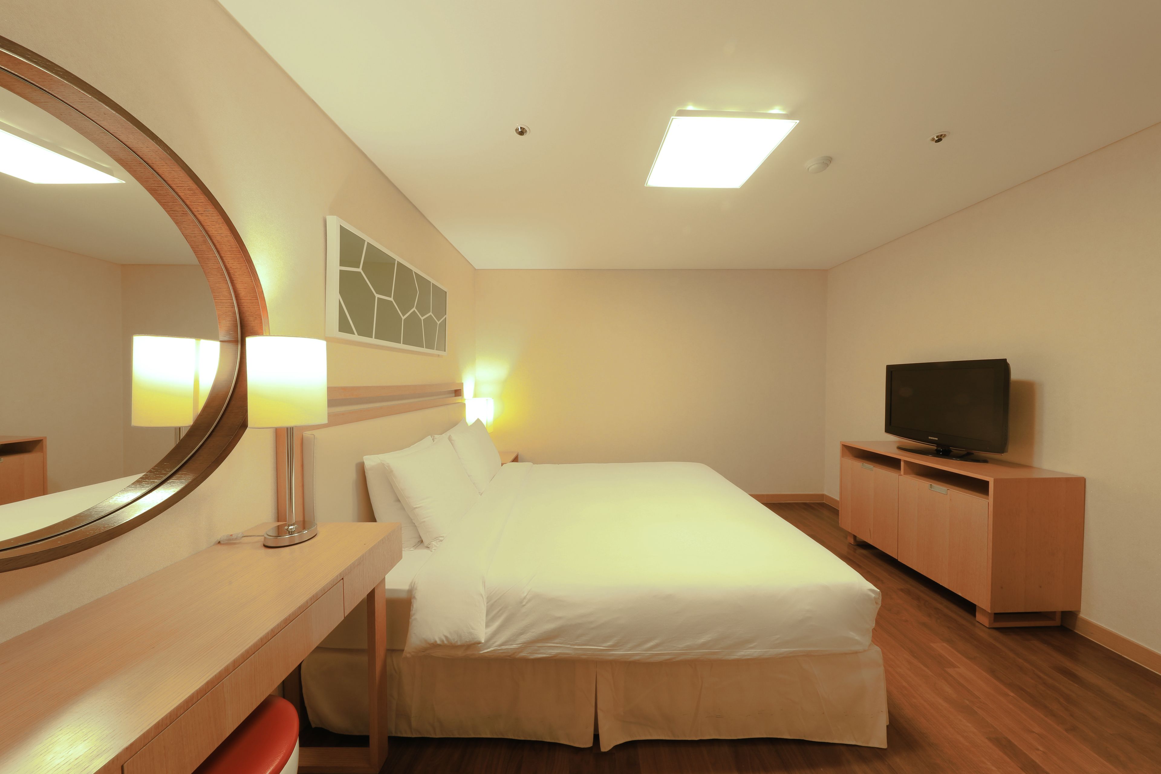 A hotel room with a bed, a TV, a desk with a lamp, and a mirror.