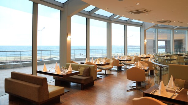 Un restaurant moderne offrant une vue sur l’océan, avec de hauts plafonds, de grandes fenêtres et un mobilier contemporain.