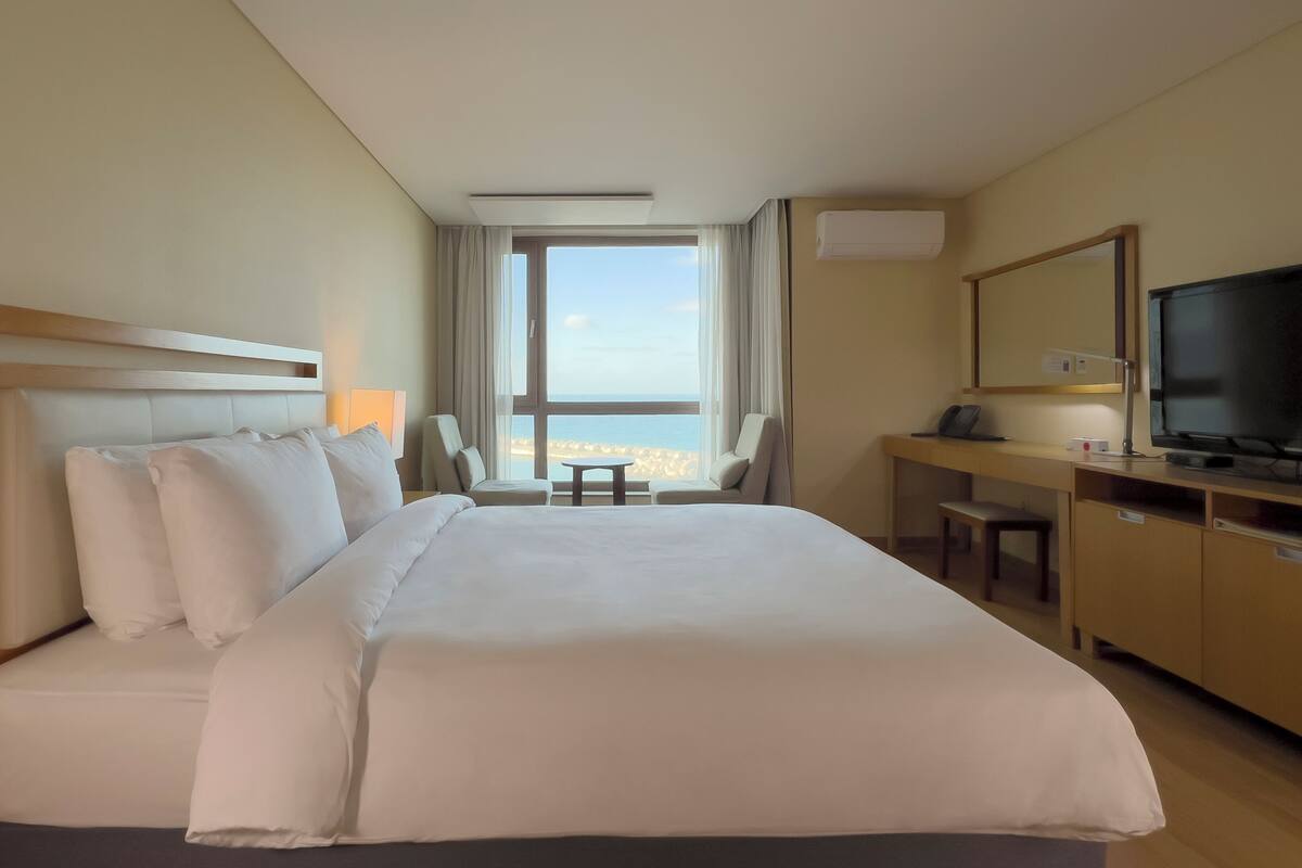 Une chambre d’hôtel avec un grand lit, un bureau avec une chaise, une télévision et une vue sur la mer.