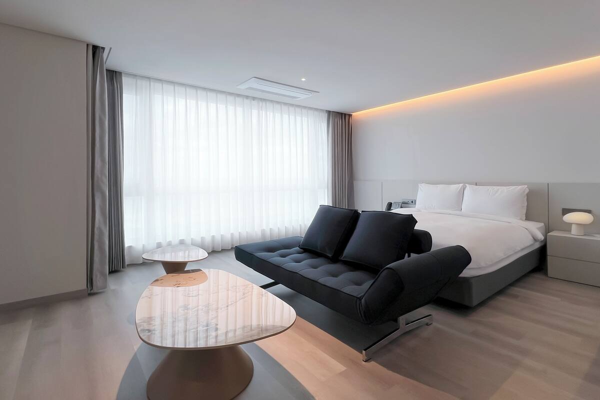 Une chambre d’hôtel moderne avec un lit, un canapé, une petite table et une lampe.