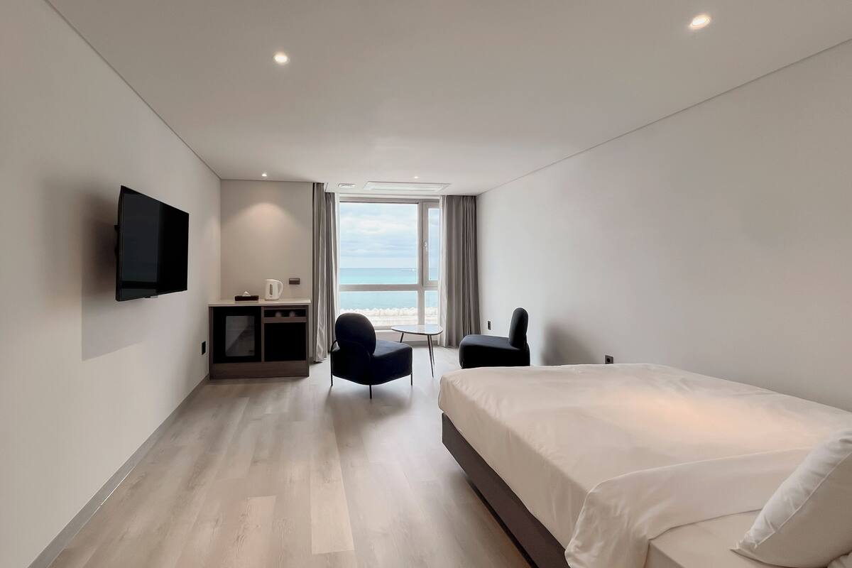 Une chambre d’hôtel moderne dotée d’un grand lit, d’un bureau, d’une chaise, d’un téléviseur à écran plat et offrant une vue sur la mer.