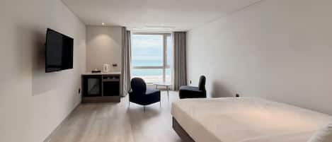 Una habitación de hotel moderna con una cama grande, un escritorio, una silla, un televisor de pantalla plana y vista al mar.