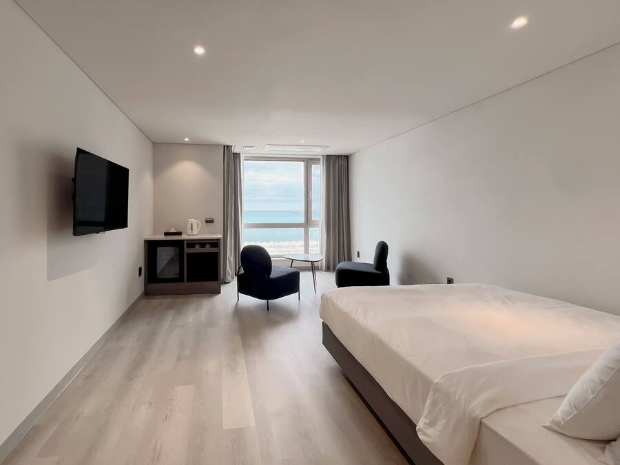 Una habitación de hotel moderna con una cama grande, un escritorio, una silla, un televisor de pantalla plana y vista al mar.