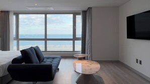 Une chambre d’hôtel moderne dotée d’une grande fenêtre donnant sur la mer, d’un lit, d’un canapé et d’une petite table ronde.