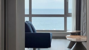 Une pièce dotée d’une grande fenêtre donnant sur la mer, d’un canapé bleu et d’une petite table ronde.