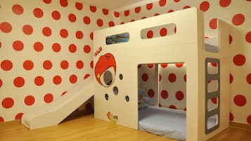 Zona infantil con tobogán, una cama pequeña y una pared con lunares rojos.