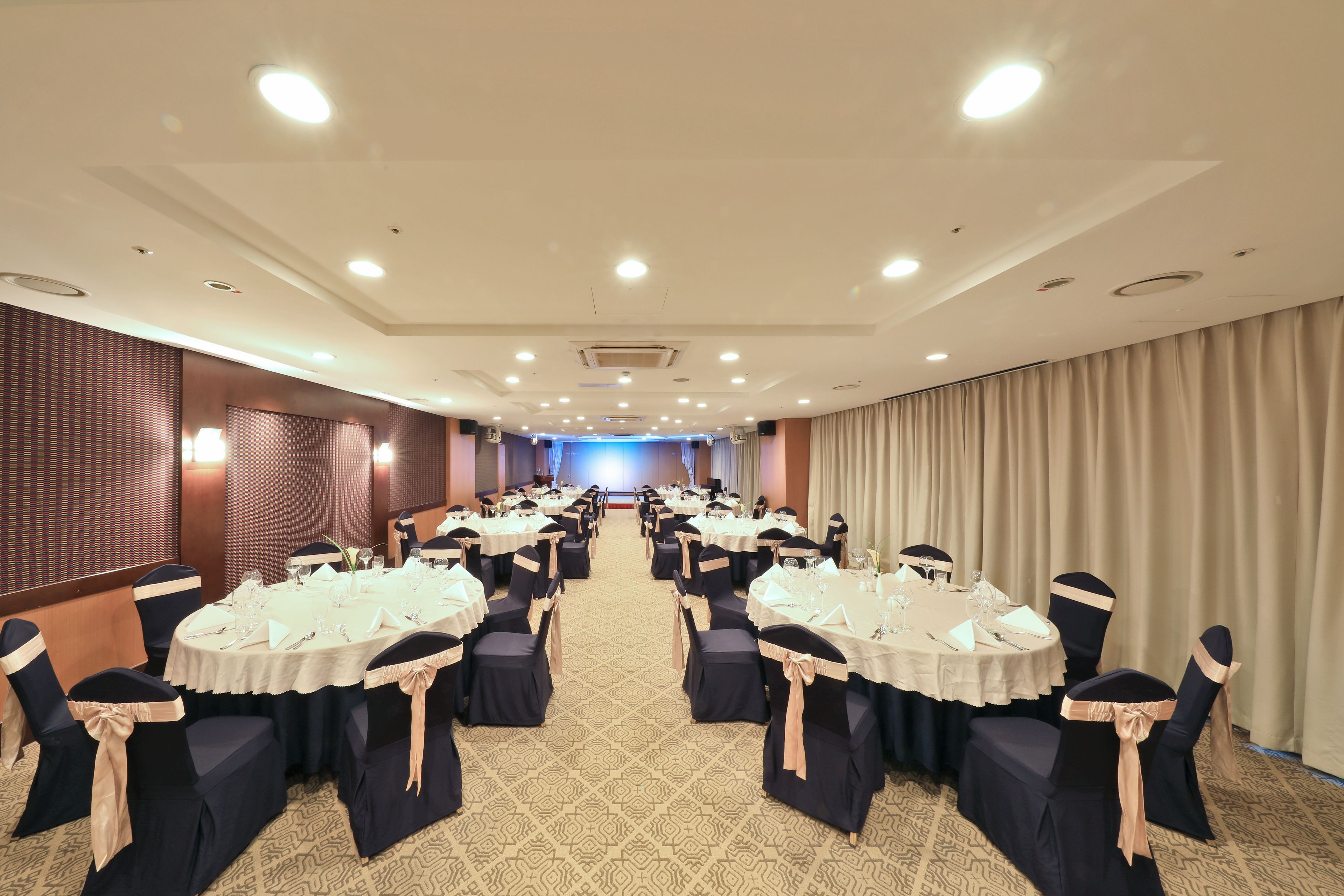 Un salón de conferencias con varias mesas redondas, cada una con mantel blanco y sillas azul marino.
