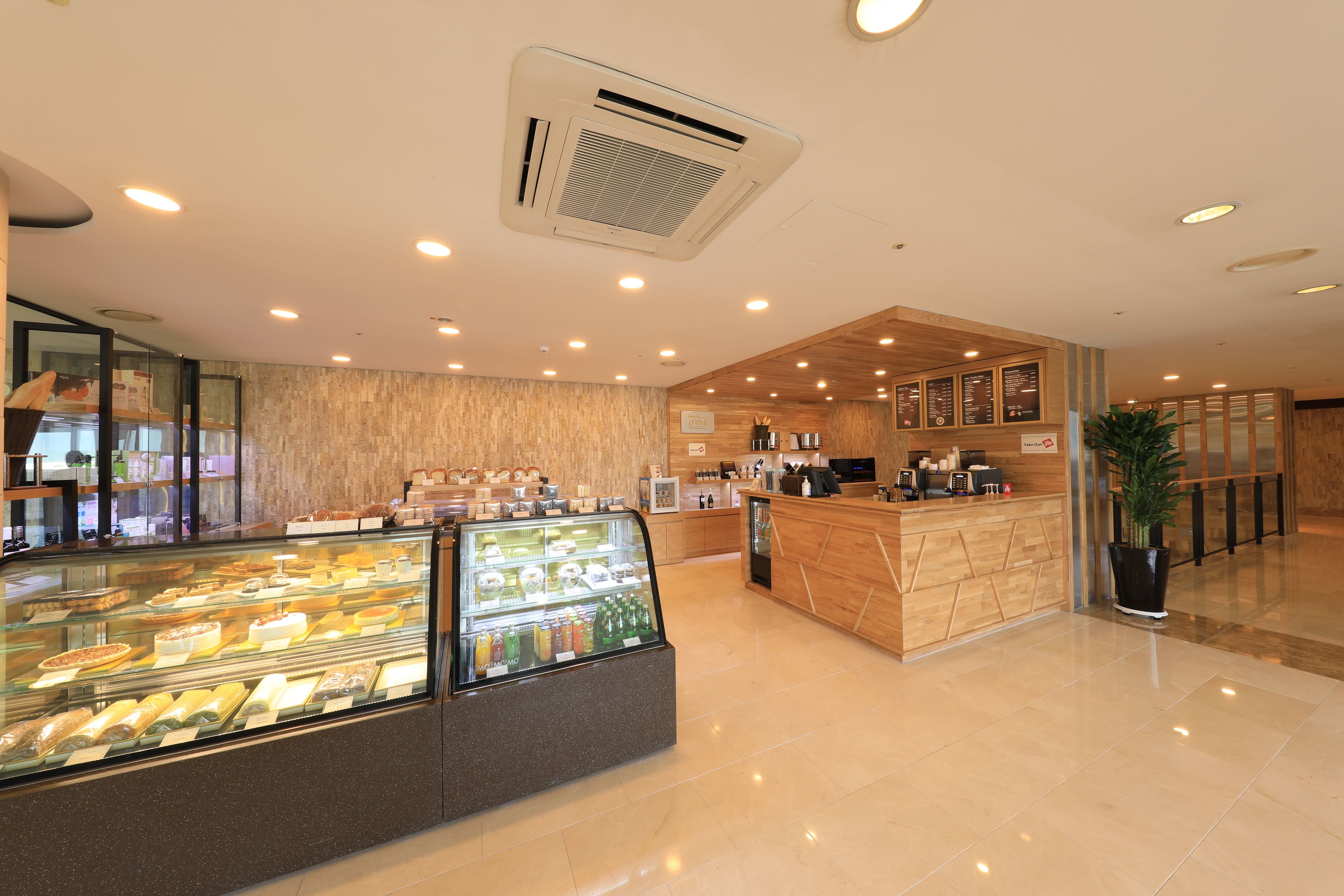 A modern hotel lobby with a bakery display, a reception desk, and a potted plant.