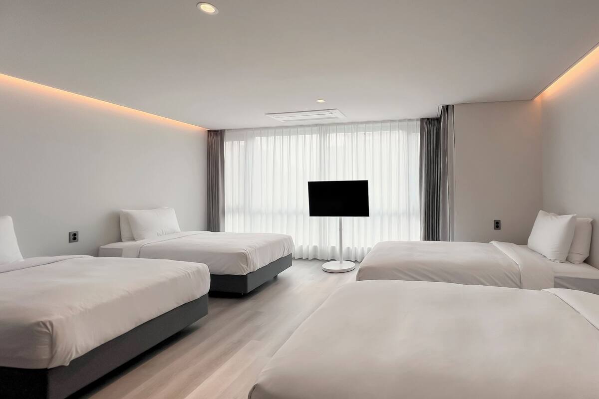 Une chambre d’hôtel moderne dotée de deux lits simples, d’un téléviseur à écran plat et d’une grande fenêtre avec des rideaux légers.