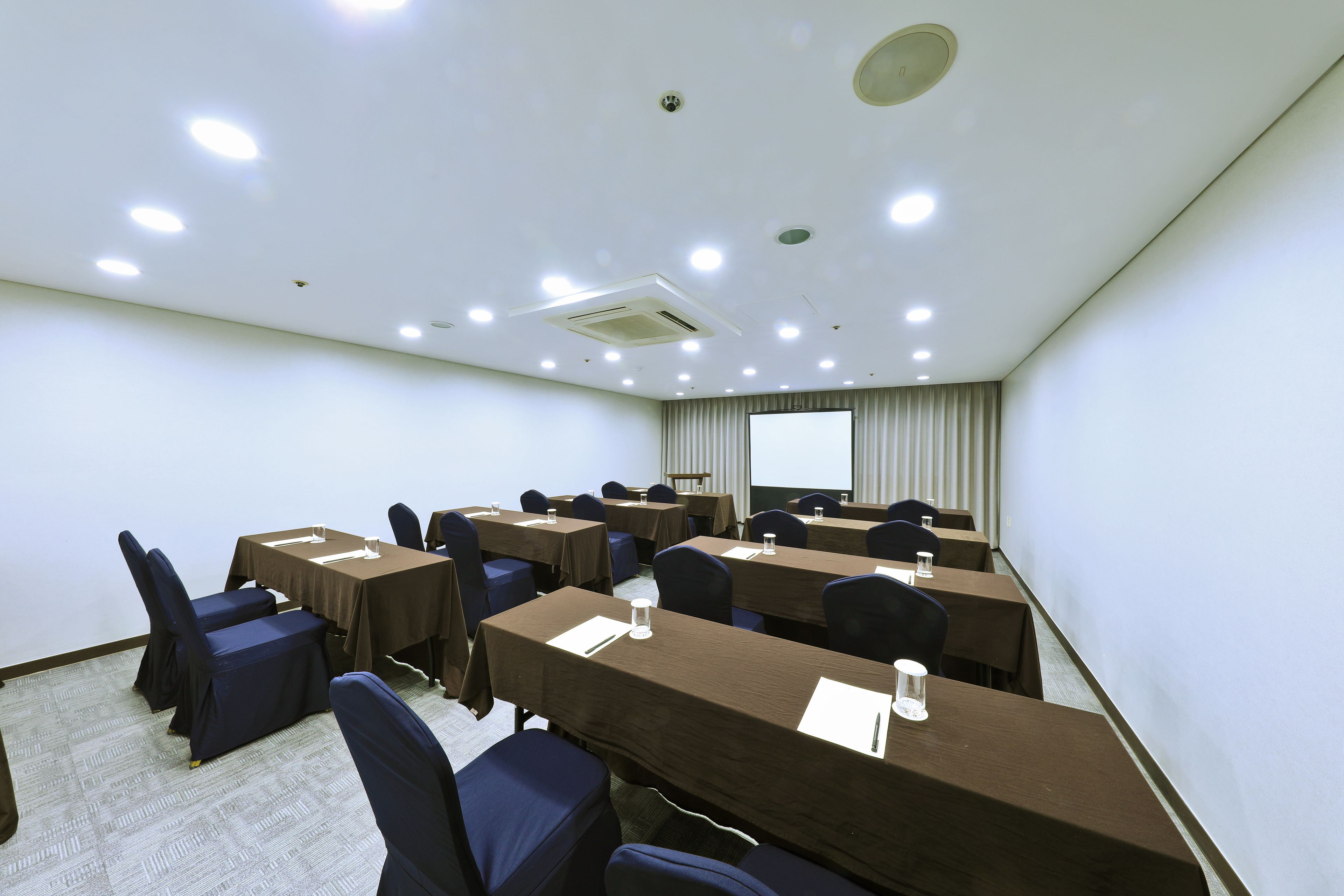 A conference room with multiple tables, chairs, and a projector screen.